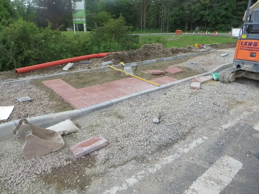 Dropped kerb crossover under construction with new kerbs, red paving blocks and a digger bucket on the sub-base